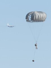 soldier falling with his parachute deployed as he passes behind the transport plane from which he...