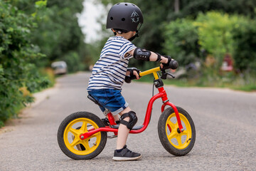 A cheerful little boy rides a running bike in a helmet outdoors. A happy child is engaged in an...