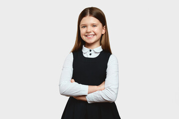 Beautiful elementary school girl in uniform with blonde hair, keeping hands crossed and looking at...
