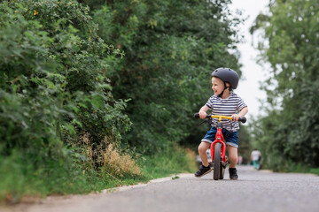 A cheerful little boy rides a running bike in a helmet outdoors. A happy child is engaged in an active sport. Protection. Life insurance and child safety.