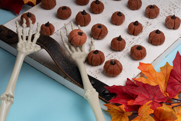 Pumpkin spiced cheesecake minis, shaped like tiny pumpkins, and topped with chocolate chips on a rustic white serving tray with skeleton hands.