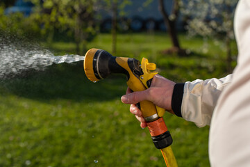 A hand of a young Caucasian man in white jacket who is watering the grass on a hot summer evening. Extremely hot weather.