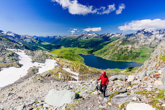 Hiker walking on mountain ridge above the blue lake Montespluga, Madesimo, Valle Spluga, Valtellina, Lombardy