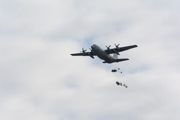 Military logistics transport plane dropping loads with parachutes, airdrop on a cloudy day
