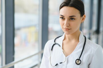 Portrait of young female doctor standing in hospital corridor. Caucasian woman working in nursing home.