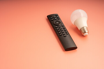 a remote control and a light bulb on a peach-colored surface