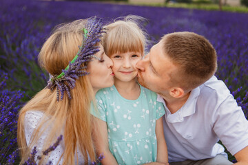 Fototapeta premium In a field of lavender, you will find a happy family kissing their little daughter