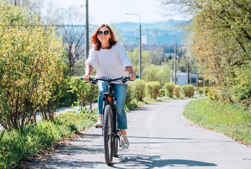 A happy smiling Caucasian woman in fancy sunglasses riding a bicycle on the city park street. Ecology sustainable transport and happy people concept image.