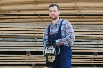 Carpenter with a saw in his hands stands on a background of cut wooden boards.