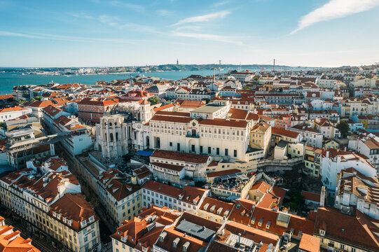 Aerial drone view of Carmo Church and surrounding historic neighbourhood in Chiado, with Tagus River and 25 April Bridge visible, Lisbon, Portugal