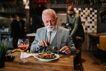 Happy businessman sitting in restaurant and having lunch. He is enjoying in delicious food and wine.