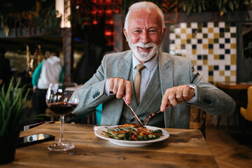 Happy businessman sitting in restaurant and having lunch. He is enjoying in delicious food and wine.