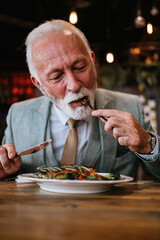 Happy businessman sitting in restaurant and having lunch. He is enjoying in delicious food and wine.