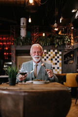 Happy businessman sitting in restaurant and having lunch. He is enjoying in delicious food and wine.