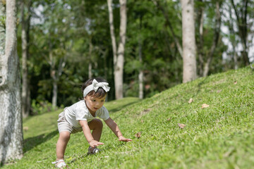 little brown girl trying to climb up the side of a small hillside covered with green grass