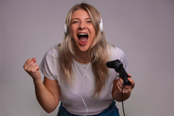 Portrait of beautiful gamer woman playing video game and using joystick and headphones on gray background © Dexon Dee