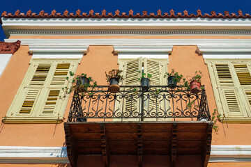 Low-angle view of a traditional house with closed wooden shutters and a balcony with plant pots against a blue sky in Nafplion, Peloponnese