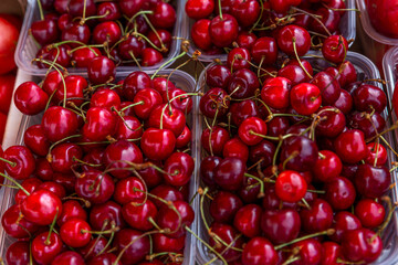 Lots of ripe cherries in containers on a market stall. Close-up. Health, vitamins and organic...