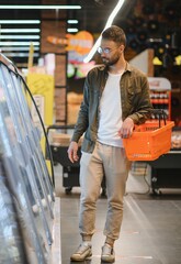 Handsome man buying some healthy food and drink in modern supermarket or grocery store. Lifestyle and consumerism concept