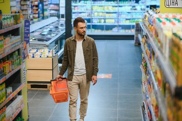 Portrait of smiling handsome man grocery shopping in supermarket, choosing food products from shelf