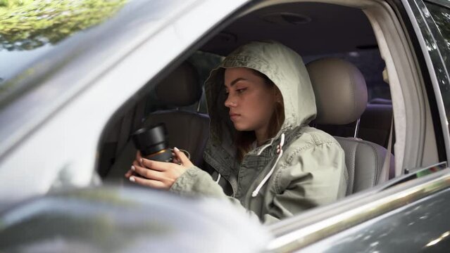 Female private detective or paparazzi with a camera sit in a car, takes photo of object of surveillance