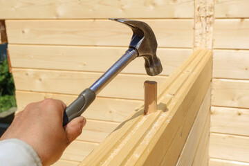 Hand holds hammer and strikes wood dowel to secure connection of wall timbers