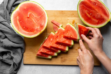 Female hands cutting fresh juicy watermelon slices on cutting board.
