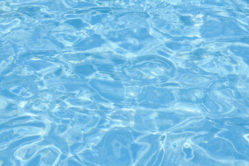Defocused blurred transparent blue colored clear calm water surface texture with ripple. Shining blue water background. Water in swimming pool.