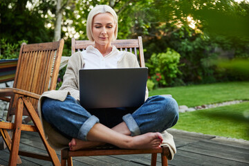 Adult woman working on laptop on house terrace during summer afternoon