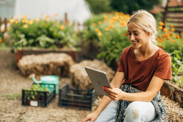 Beautiful woman sitting on a hayrick in her garden and using a digital tablet.