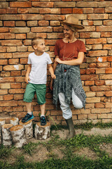 Front view of a woman and her son standing on a tree stomps in front of the brick wall.
