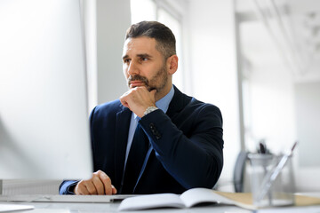 Busy middle aged entrepreneur man working on computer in office, looking at monitor, reading news or corporate emails