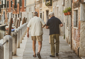 Fototapeta na wymiar Two italian senior men walking on the cobblestone narrow streets in Venice, Italy