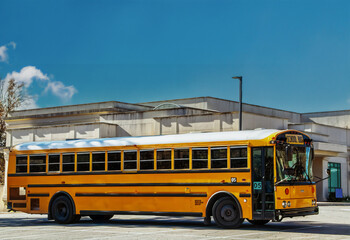 Large capacity yellow school bus from USA parked by building on bright day