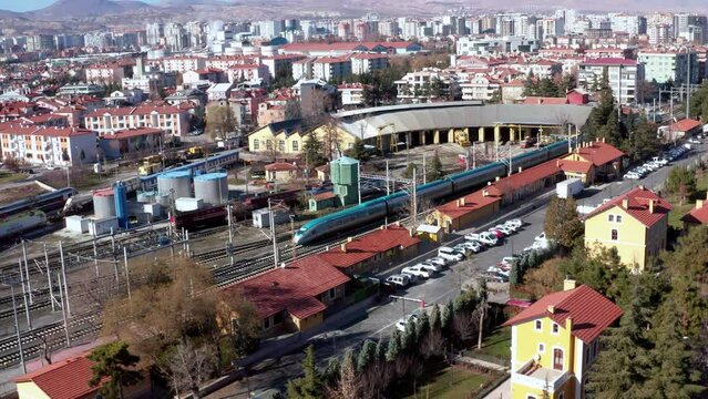 4K wide angle panoramic drone shot of train station in daylight with cityscape in the background. Footage of arriving high-speed passenger train at green-roofed platforms stock video.