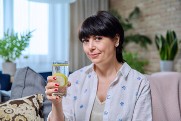 Smiling mature woman relaxing at home with glass of lemon water