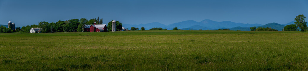 landscape with grass and sky Vermont countryside panorama rural red barn with lush green fields another side of Lake Champlain the Adirondack mountains are hazy from Canadian forest fires 
