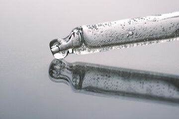 Cosmetic pipette with vitamin C with air bubbles on mirror background.