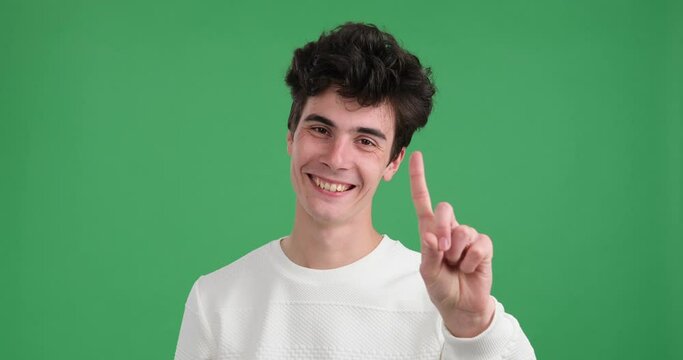Sly Caucasian man over green background wagging his finger in a teasing manner. With a mischievous glint in his eyes and a playful smile on his face, he conveys a sense of cunning and cleverness.