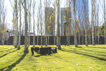 Young man doing push-ups on a grass in the park. Copy space.