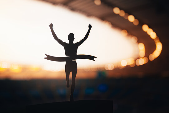 Silhouetted Runner Claims Victory at Modern Athletics Stadium. Edit Space, Track and Field Competition Photo. Warm orange edit space