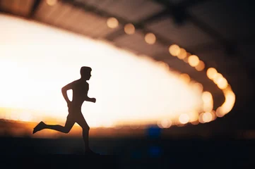 Foto op Plexiglas Silhouette of a Male Athlete, a Long-Distance Runner, Against the Beautifully Illuminated Backdrop of a Modern Sports Stadium © kovop58