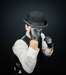 Portrait of Vintage Back Alley Pugilist in Vest and Bowler Hat Standing in Fighting Position. Mobster in Black Leather Gloves.