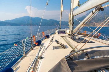 Stoff pro Meter Yacht sailing in an open sea. Close-up view of the deck, mast and sails. Clear sky, waves and water splashes © dtatiana