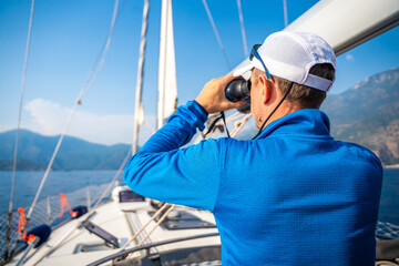 Young man captain on the yacht looking through binoculars during sailing boat control. Travel and active life.