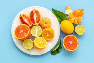 Plate full of fresh citrus fruits with green leaves, top view