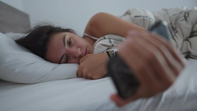 Woman staring at phone screen in the morning bed. Sad depressed female person unable to wake up from bed reading message online holding smartphone
