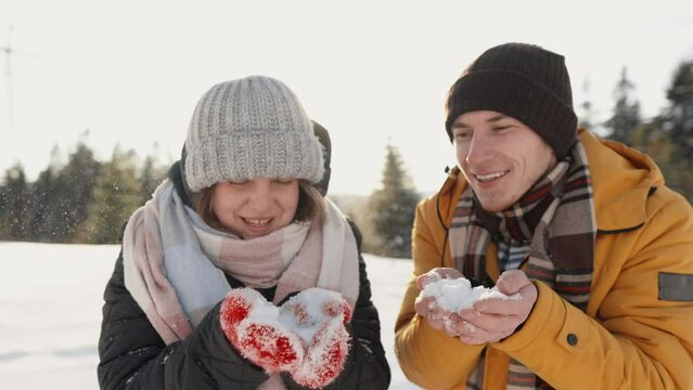 Young happy couple in love blows snow from palms to camera in winter. Man and woman give winter mood and magical fairy tale anticipation holiday Christmas and new year. Congratulations on first snow