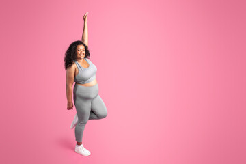 African american plus size lady in sportswear enjoying result of workout, standing on pink background, free space