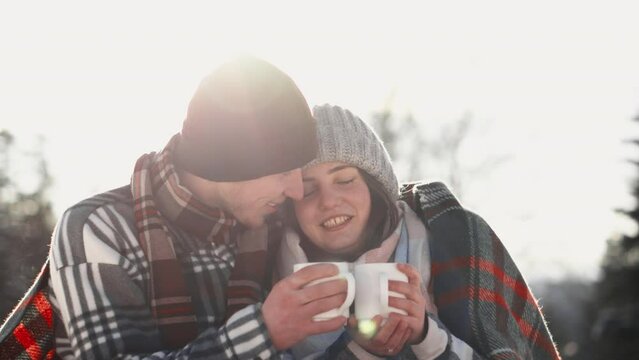 A fascinating shot shows a young family reliving moments of warmth of a delicious hot drink and enjoying the tranquility of a sunny winter day. Camping together
